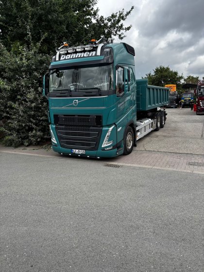 Grüner Muldenkipper-Lkw der Marke Volvo mit der Aufschrift „Dahmen“ auf dem Dach, auf einem Parkplatz neben einer Straße, bei bewölktem Himmel.