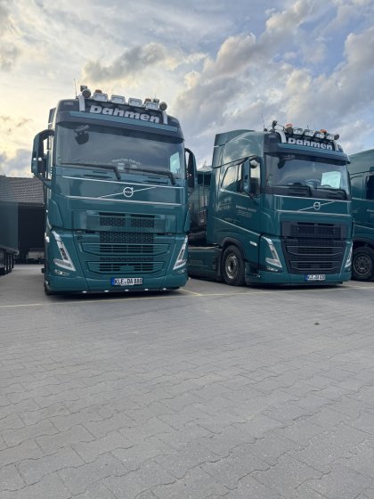 Zwei grün lackierte Volvo-Sattelzugmaschinen mit dem Firmenschriftzug "Dahmen" stehen nebeneinander auf einem gepflasterten Parkplatz unter bewölktem Himmel.