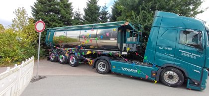 Blauer Volvo-Sattelzug mit verchromtem Tankaufleger, geschmückt mit bunten Wimpelketten, steht auf einem gepflasterten Weg neben Bäumen und einem Verkehrsschild „Durchfahrt verboten“.